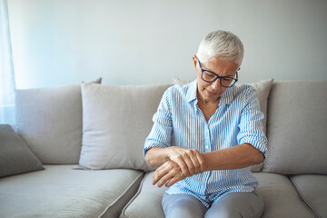 Photo of Elderly lady is enduring strong ache while sitting on the sofa during the day. Senior Woman At Home Suffering With Arthritis. Upset stressed mature middle-aged woman feeling pain ache.