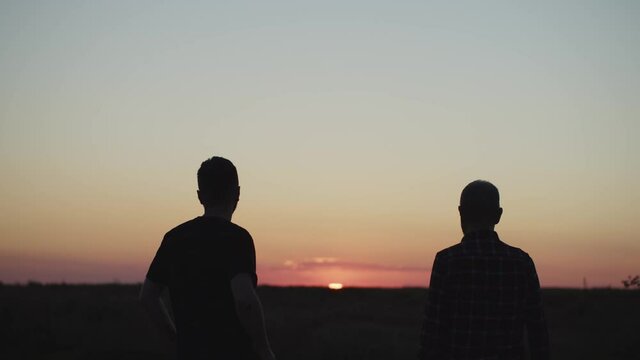 Silhouette of senior father and young son accompanying purple sunset hugging each other with love. Family communication. Friendsheep. Peaceful mood. Parenting concept. Human aging. True feelings. 4K