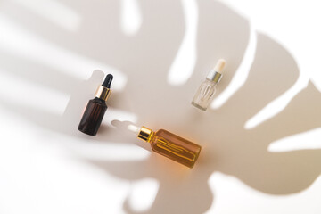 White, orange and black serum bottles on white background. Trending shadow from a palm branch. Cosmetic mockup. Place to insert text, images. Top view. Flat lay.