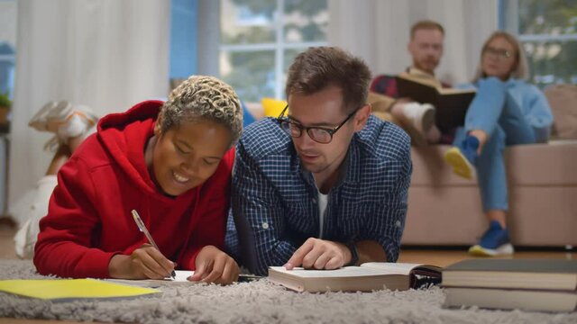 Happy multiethnic students preparing for exams together lying on floor in dorm room