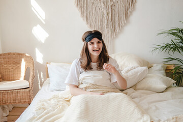 Obraz premium Young beautiful womanlying in comfortable bed and mask for sleep in the morning at cozy home. Self-isolation, stay home during quarantine, pandemic.