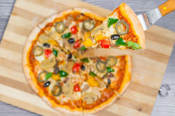 Close up and top view of Chicken mushroom jalapeno pizza slice lifted from wooden cutting board.