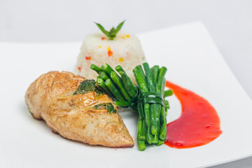 Pan roasted chicken breast with long green beans and light vegetable rice platter. Food decorating with red sauce on a white plate. Isolated white background.
