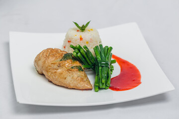 Pan roasted chicken breast with long green beans and light vegetable rice platter. Food decorating with red sauce on a white plate. Isolated white background.