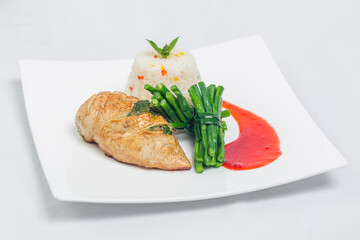Pan roasted chicken breast with long green beans and light vegetable rice platter. Food decorating with red sauce on a white plate. Isolated white background.