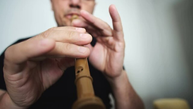 Close-up of a man playing on a recorder on a blur background, wooden wood flute