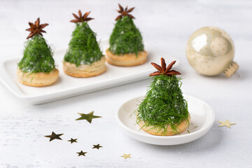 Christmas snack in the form of trees. Delicious cream cheese canapes with nuts, garlic and chopped dill on homemade puff cookies, decorated with a anise star. on light gray background