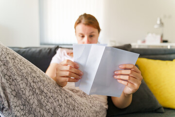 Fototapeta na wymiar Low angle view on caucasian woman sitting at home on the sofa bed opening envelope with letter in day - Leisure activity receiving contract greeting card or invoice concept