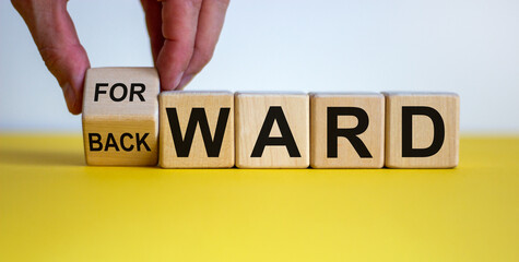 Hand turns a cube and changes the word 'backward' to 'forward' on wooden cubes. Beautiful yellow table, white background, copy space.