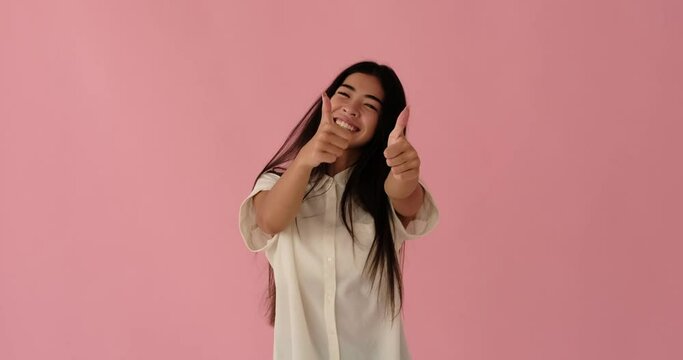 Cheerful korean woman giving thumbs up gesture with both hands over pink background