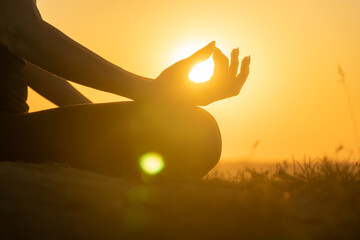 Silhouette of hand of a woman meditating in a yoga pose on nature at sunset