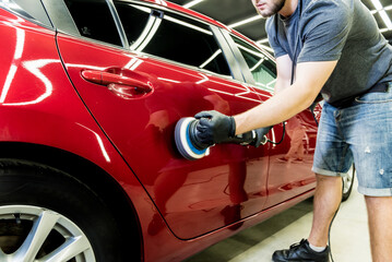 Car service worker polishes a car details with orbital polisher.