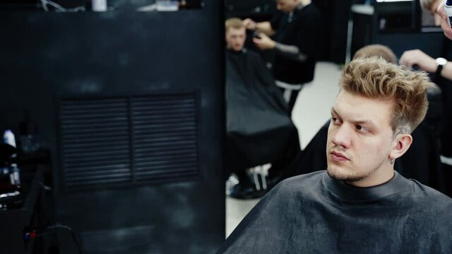 Attractive male is getting a modern haircut in barber shop. Barber dyes hair to the client with a blue spray.