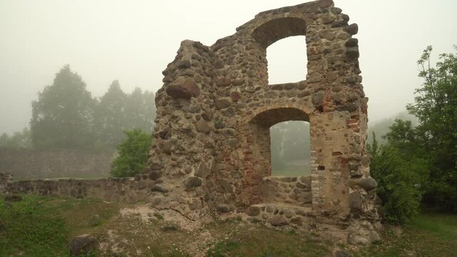 A fragment of the medieval stone wall structure with window arches in a territory of the Livonian Order stone castle ruins in Dobele, Latvia. The beautiful, foggy morning landscape in summer.