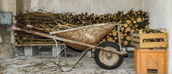 old rusty wheelbarrow against pile of hazel tree firewood