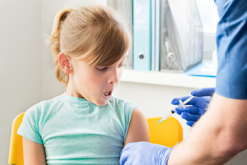 Little girl in face mask in doctor's office is vaccinated.Crying, scared, afraid of syringe with vaccine for covid-19 coronavirus,flu,infectious diseases.Clinical trials of injection for human, child