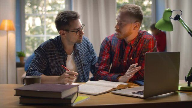 Cool students studying with books and laptop in dorm living room