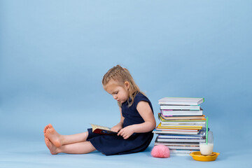 Fototapeta premium Girl is sitting on a books pile and enjoying her reading. 