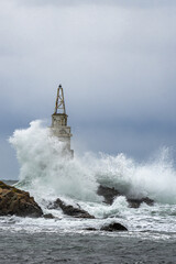 Tall lighthouse in the stormy ocean under dark storm clouds