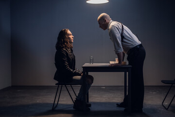 A white male police detective talks to a suspect in a drug trafficking case who is sitting in an...
