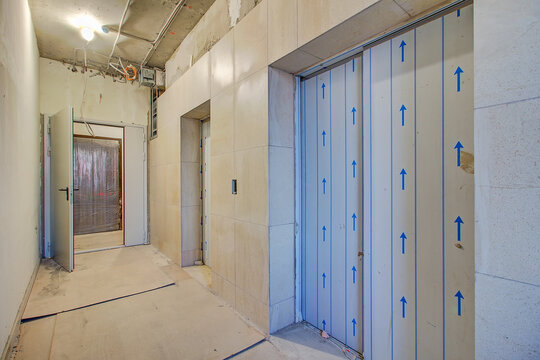 Finishing work. Patching and plastering work to newly installed drywall in new construction. Light white yellow corridor modern elevator with doors is closed.  Inexpensive, economical interior.