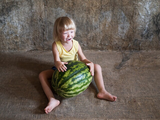 Fototapeta premium Funny blond boy sitting near big watermelon lying on floor
