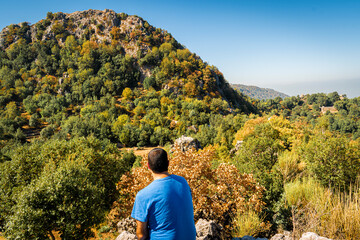 Young man sitting on top of cliff in summer mountains at sunrise and enjoying view of nature