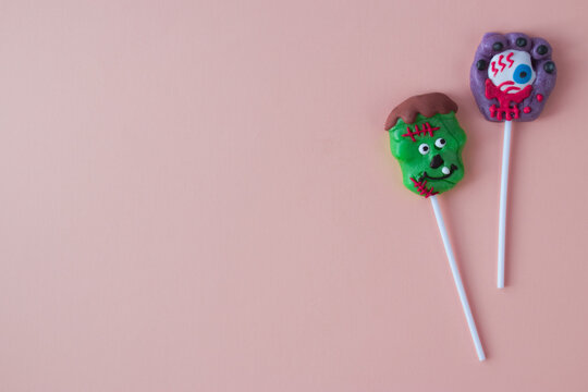 Two scary heluin lollipops lie on a pink background.