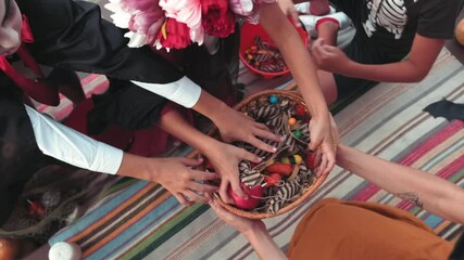Handheld top view shot of kids in halloween costumes grabbing candy from basket held by woman