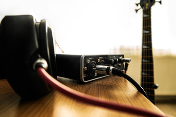 Headphone and soundacard on the table and a bass guitar on the background.