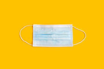 Surgical mask with rubber ear straps on yellow background.