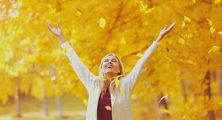 Happy smiling woman and flying yellow leaves in autumn park