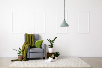 Interior of room with stylish armchair and houseplants near white wall