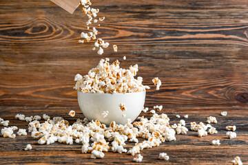 Throwing of tasty popcorn into bowl on wooden background