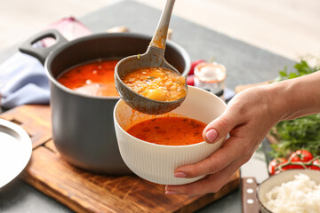 Woman pouring tasty rice soup from pot into bowl