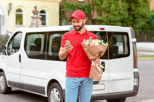 Delivery Man With Bouquet Of Beautiful Flowers And Mobile Phone Near Car Outdoors