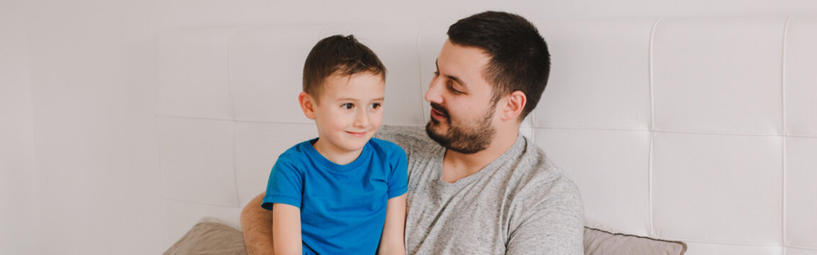 Caucasian Father Talking To Boy Son. Man Parent Hugging Kid Child At Home. Authentic Lifestyle Real Family Candid Moment. Happy Fathers Day Holiday. A Serious Talk. Web Banner Header.