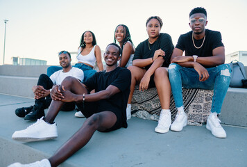 Group of young modern african black friends happily sitting together on the bench of the stairs in bright sunlight enjoying summer vacation