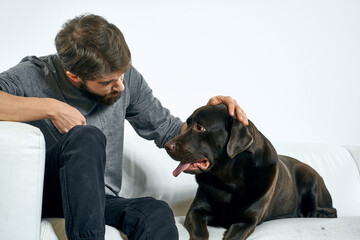 man with a black dog on a white sofa on a light background close-up cropped view pet human friend emotions fun