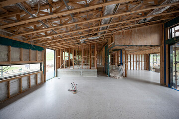 Interior view of a modern house undergoing construction, with timber frames, sliding glass doors and trusses