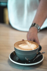 Barista offering latte with decorative leaf on foam milk
