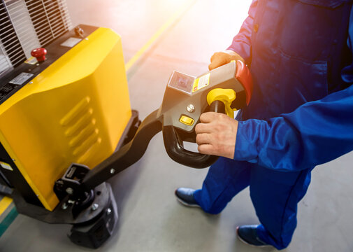 A worker in a warehouse uses a hand pallet stacker to transport pallets.