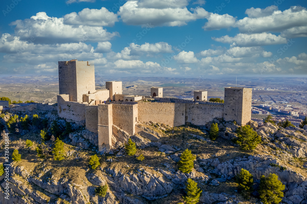 Wall mural Dreamy cloudy sky above Jaen medieval Gothic castle and parador on an outcrop of a steep hill towering over the largest olive grove in the world