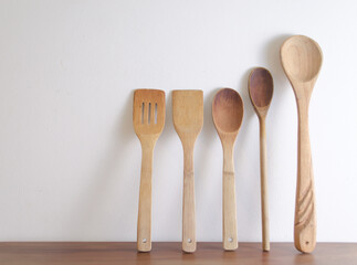 Five wooden spoons on wooden table against white wall.