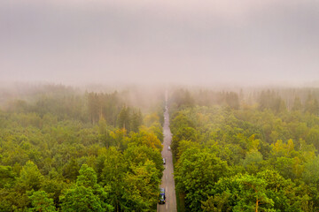 Aerial view at the car traffic on a road between a forest in foggy conditions, nice misty view from the birds eye.