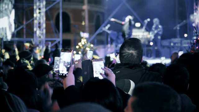 A crowd of people watch a new year celebration pary concert and record footage and shoot pictures with smartphones