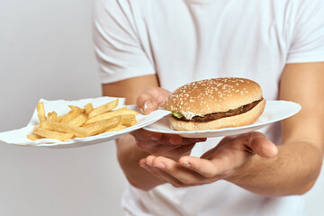 a man with fries and a hamburger on a light background in white t-shirt close-up cropped view Copy Space Model