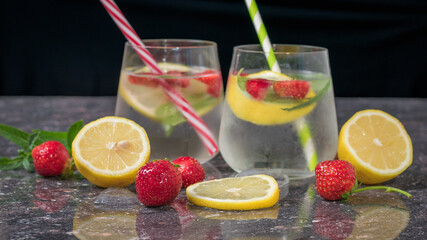 Fresh strawberries and lemon slices on the background of two glasses with a cooling drink. Selective focus.