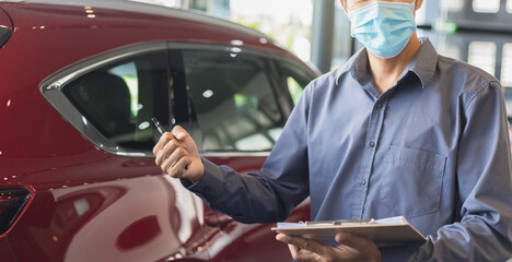 Asian saleman wear surgical mask working in inspector checking writing on clipboard in garage of dealership Wait mechanic In showroom car and insurance new normol covid-19 in showroom dealership