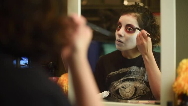 Mujer joven mexicana latina maquillaje catrina calavera d&iacute;a de muertos halloween frente al espejo tradicional festividades colorido esqueleto cara rostro blanco close-up